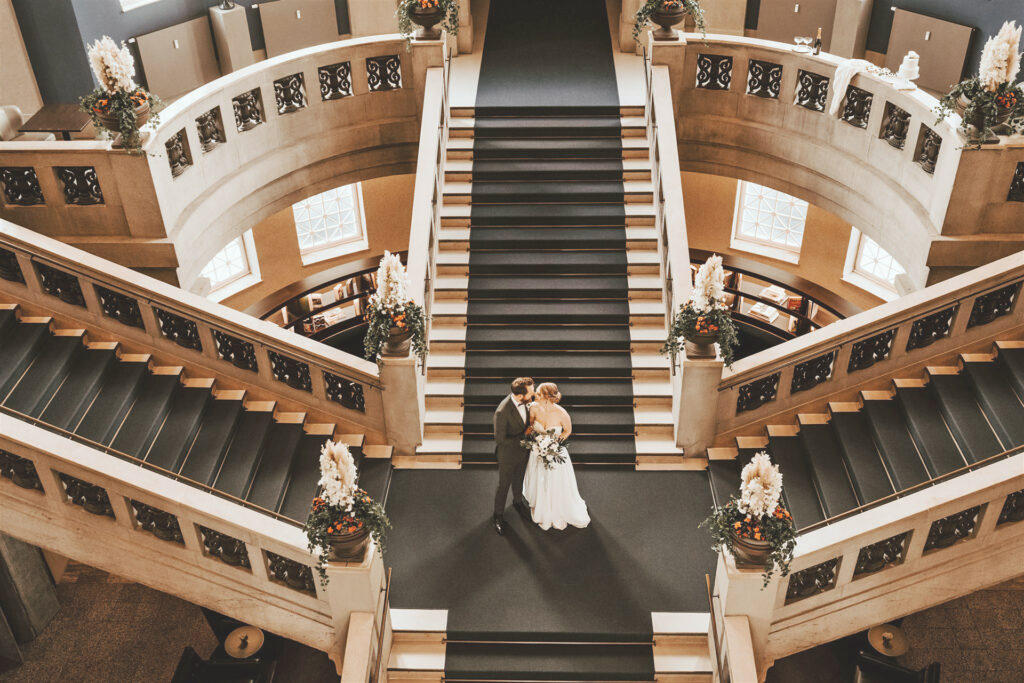 Wedding photo on the historic staircase at Hotel THE WELLEM Düsseldorf with elegant bridal couple and festive floral decorations in impressive neoclassical architecture.