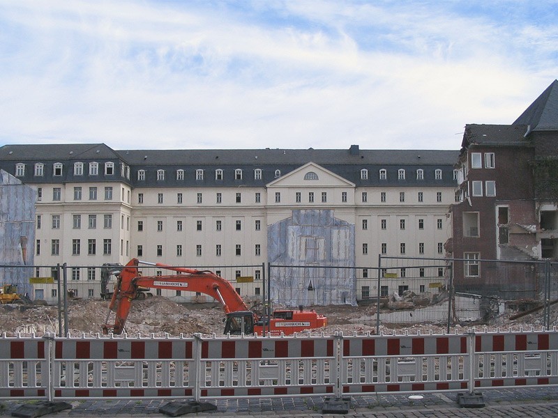 Baustellenszene vor einem historischen Gebäudekomplex in Düsseldorf mit Abrissarbeiten, Bagger und abgesperrtem Bauareal.
