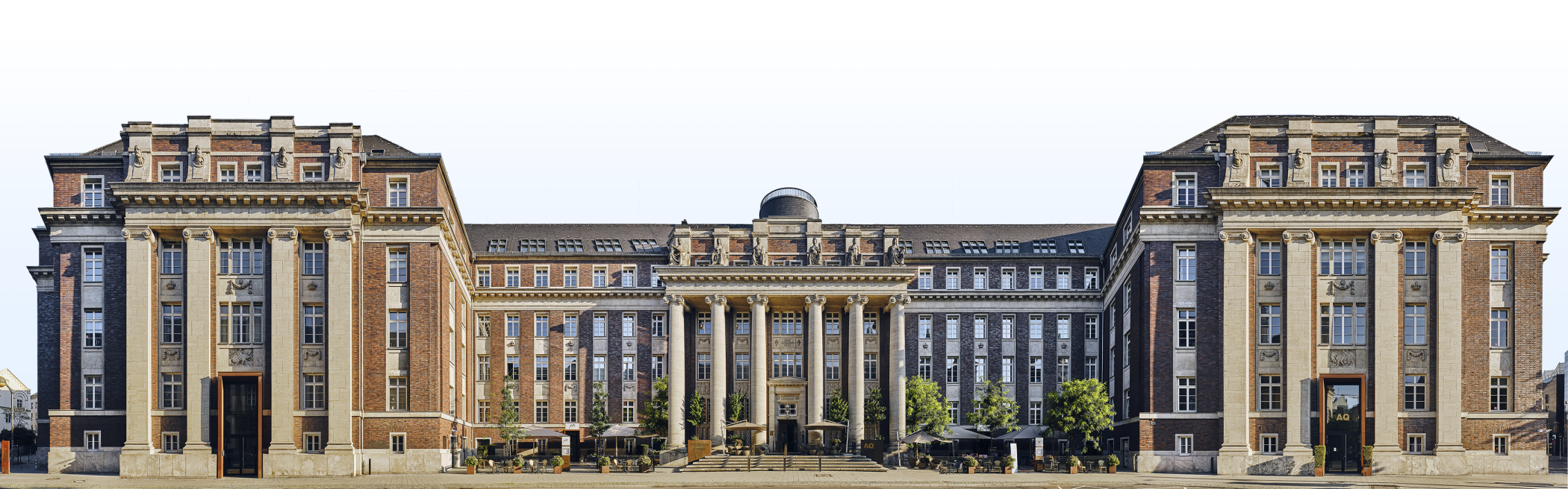Panoramafotografie der historischen Fassade des Luxushotels The Wellem in Düsseldorf mit monumentalen Säulen, symmetrischer Architektur und klassizistischen Details bei klarem Tageslicht.
