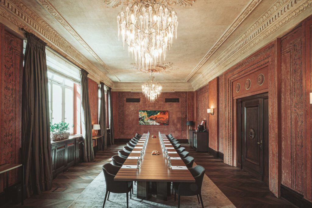 Prächtiger Salon im Hotel The Wellem in Düsseldorf, ehemaliges Richterzimmer, mit langem Konferenztisch, Kristallkronleuchter, historischen Wandverzierungen und moderner Kunst für exklusive Meetings und Events.