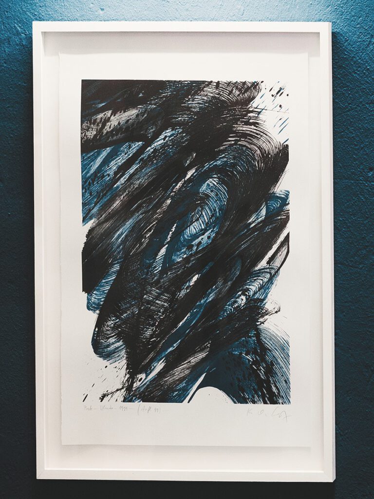 Gerahmtes abstraktes Kunstwerk im Hotel The Wellem Düsseldorf mit dynamischen schwarzen und blauen Farbstrukturen vor einer blauen Wand.