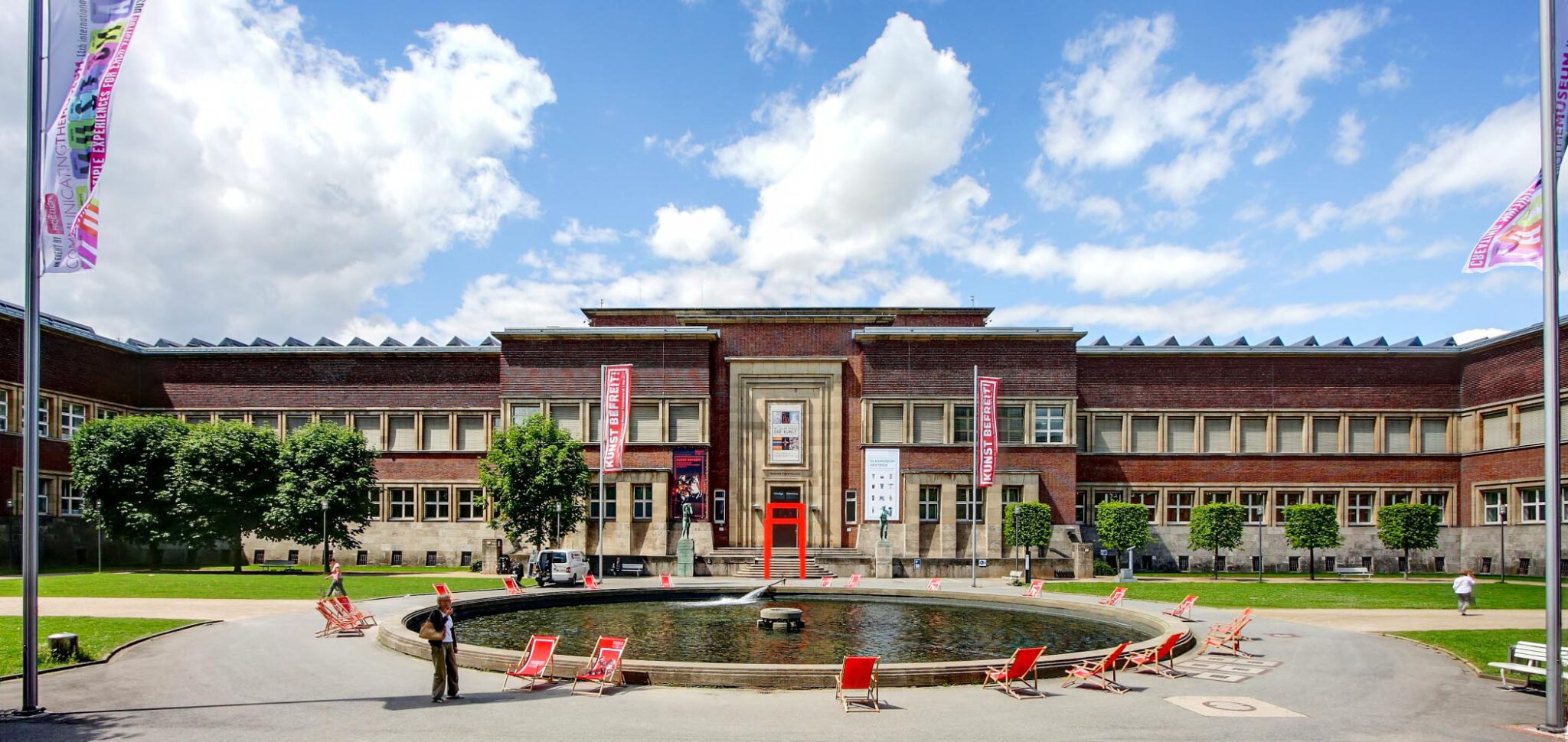 Außenansicht des Kunstpalastes in Düsseldorf mit Brunnen, Liegestühlen und weitläufigem Vorplatz bei sonnigem Wetter nahe dem Hotel The Wellem
