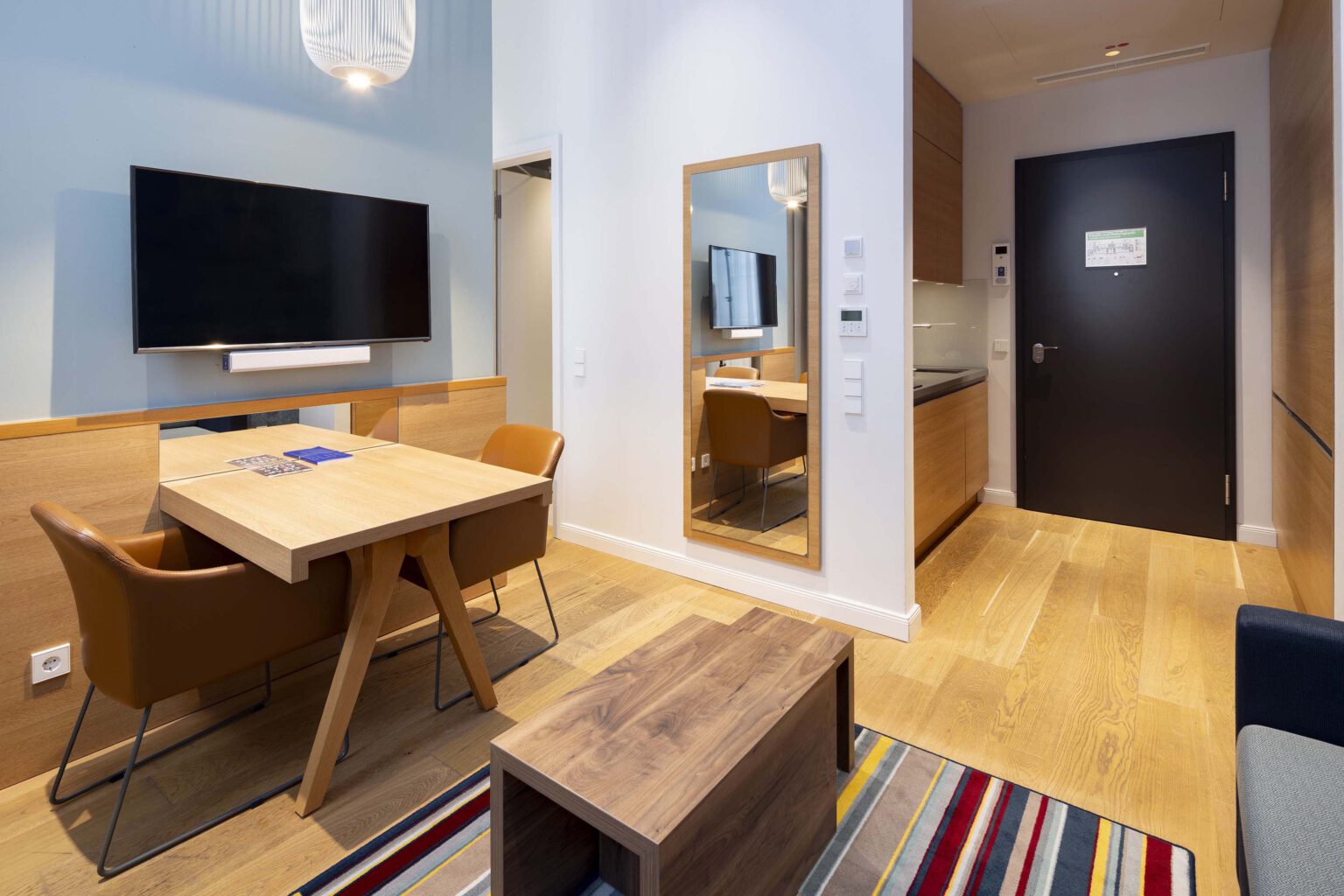 Modern studio in Hotel The Wellem Düsseldorf with dining and work area, large wall mirror, bright kitchenette and high-quality wooden interior.