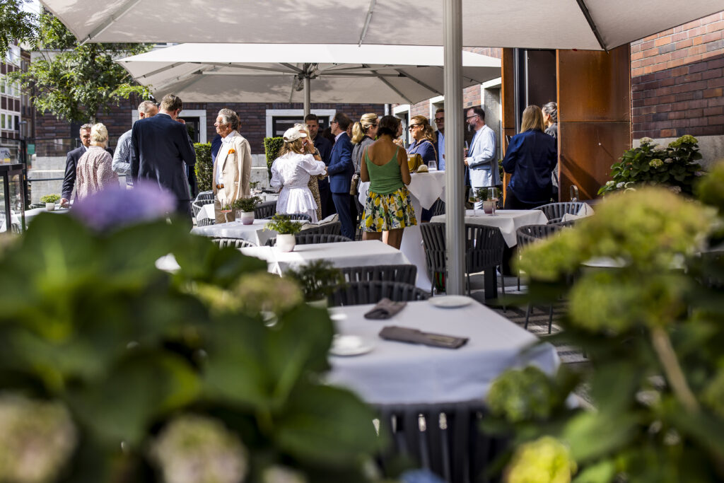 Summer get-together on the terrace of the restaurant at Hotel The Wellem Düsseldorf with elegantly dressed guests under large parasols.
