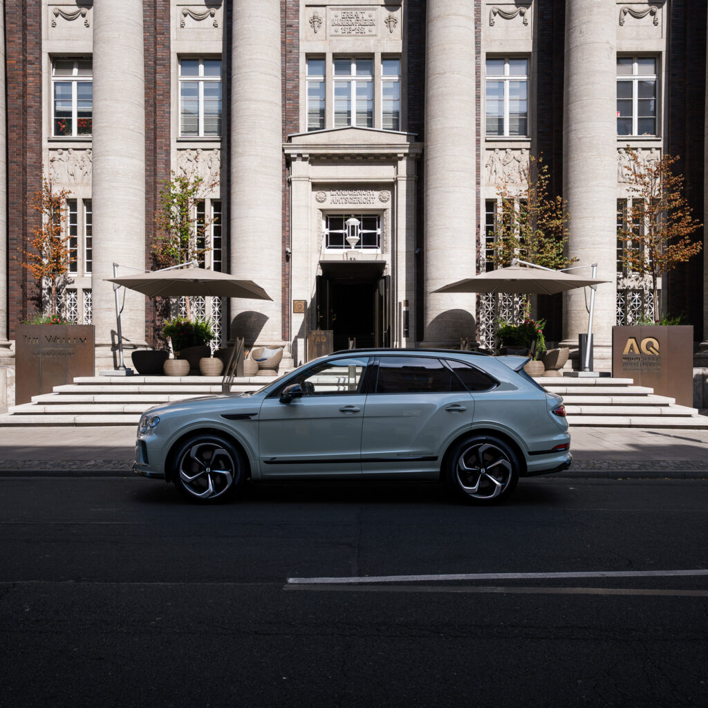 Luxury SUV in front of the impressive pillared portal of The Wellem Hotel in Düsseldorf, flanked by large parasols and elegant exterior design.